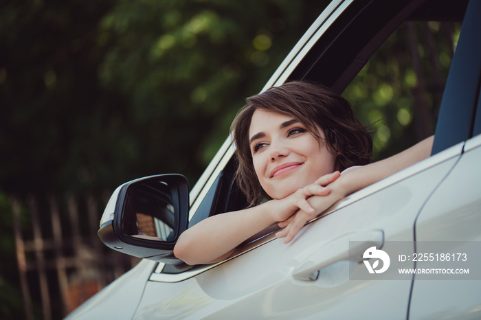 Photo of charming lovely lady smiling face hands chin dreamy inspired look out of new car rearview mirror handle relaxing enjoying natural view breathe fresh air wear white shirt indoors