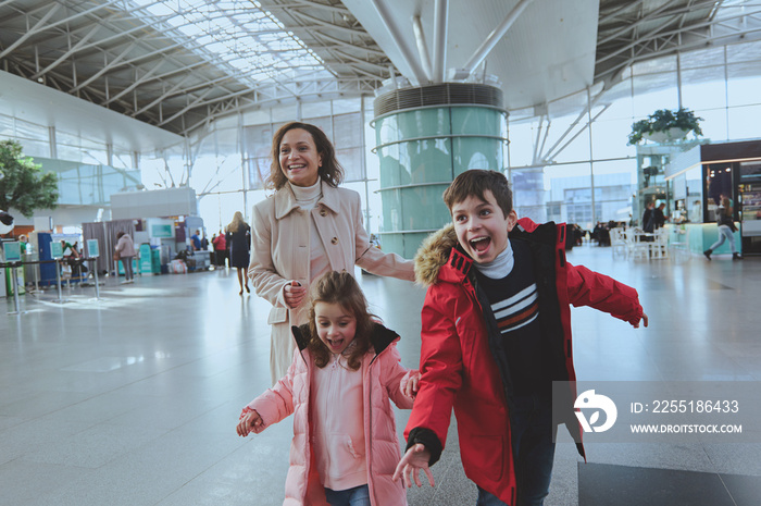 Happy multiethnic woman with her kids running in airport arrivals terminal waiting room. Long-awaited family reunion concept