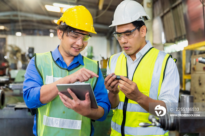 A skilled mechanic in a metal lathe is checking parts on a tablet. Engineers are working and repairing machines in industrial.