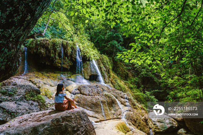 Woman relaxing on stone with waterfall at erawan national park in thailand.