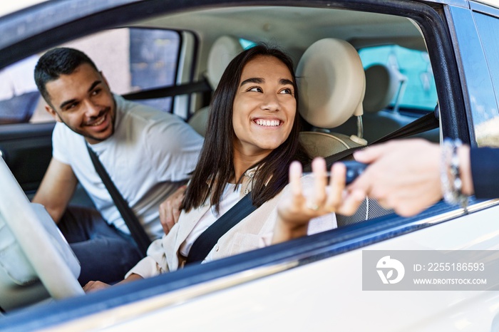 Young hispanic couple driving auto at the city. Girl smiling happy holding key of new car.