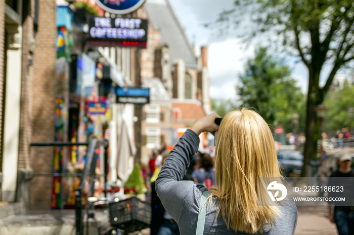 Young woman takes pictures in vacation spent in Amsterdam with beautiful architecture and coffee shop.