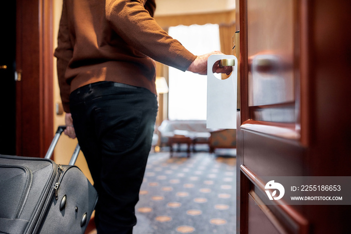 Make Yourself at Home. Cropped shot of middle-aged businessman in casual wear with suitcase entering his room. A door with a sign.