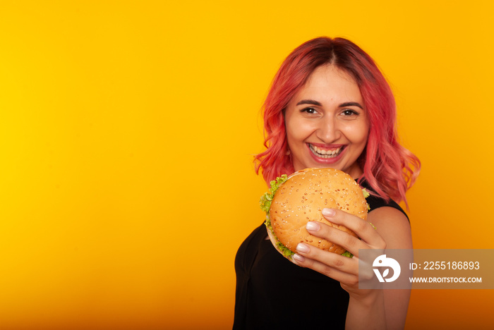 a woman with bright pink hair shows a delicious burger with a smile on her face charming. Advertising fast food, I love junk food. vs vegans. Vegan Burger Without Meat. space for text