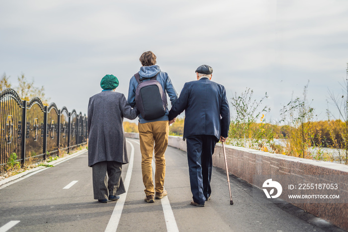 An elderly couple walks in the park with a male assistant or adult grandson. Caring for the elderly, volunteering