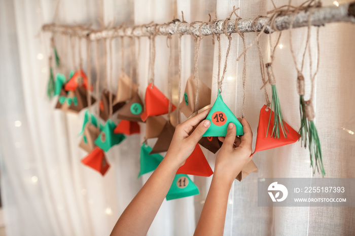 Kid opening handmade advent calendar with color paper triangles. Seasonal activity for kids