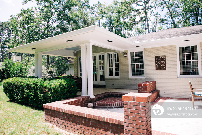 Back Rearview of exterior white cream brick 1950’s house with black shutters and a large porch patio and also with a lawn lot with curb appeal