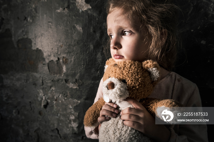 upset kid holding teddy bear in dirty room, post apocalyptic concept