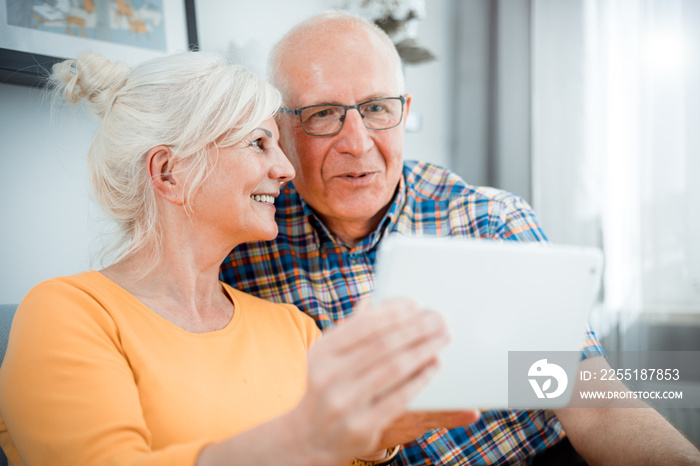 Happy senior couple looking at tablet sitting on sofa at home