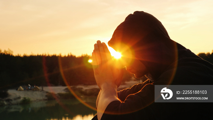 The young man folded his hands in prayer, sitting at sunset in the hood