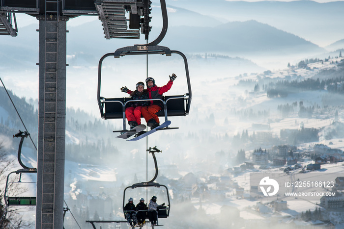 Couple snowboarders having fun on a ski lift in ski resort with beautiful background of snow-covered slopes, forests, hills copyspace recreation travelling tourism vacation mountains Bukovel, Ukraine