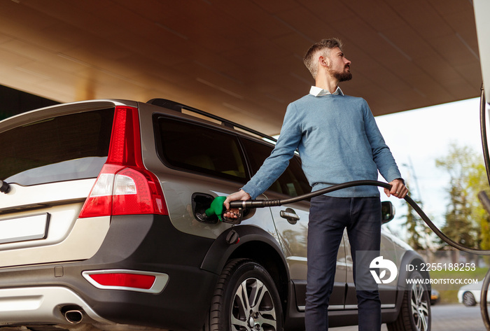 Bearded man refueling car and looking away