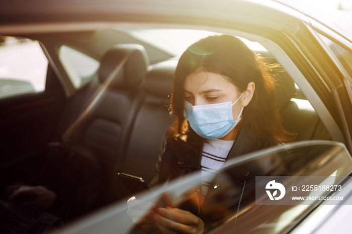 Girl in protective sterile medical mask on her face is  talking on his phone in taxi. The concept of preventing the spread of the epidemic and treating coronavirus, pandemic in quarantine city.