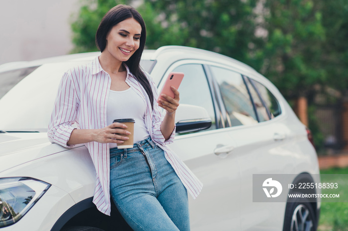 Photo of positive cheerful girl ride drive car stop break pause buy barista takeout coffee beverage mug use smartphone read social network news in city center outside