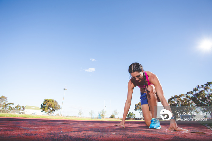 Female fitness model and track athlete sprinting on an athletics track made from tartan