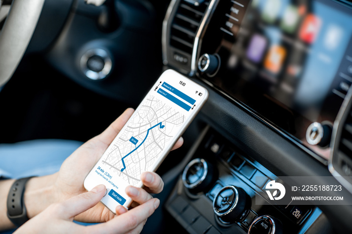 Close-up of a smartphone with navigation app in the modern car with monitor on the background