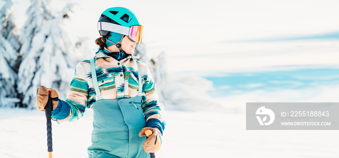 Woman in skiing clothes with helmet and ski googles on her head with ski sticks. Winter weather on the slopes. On top of a mountain and enjoying view. Alpine skier. Winter sport