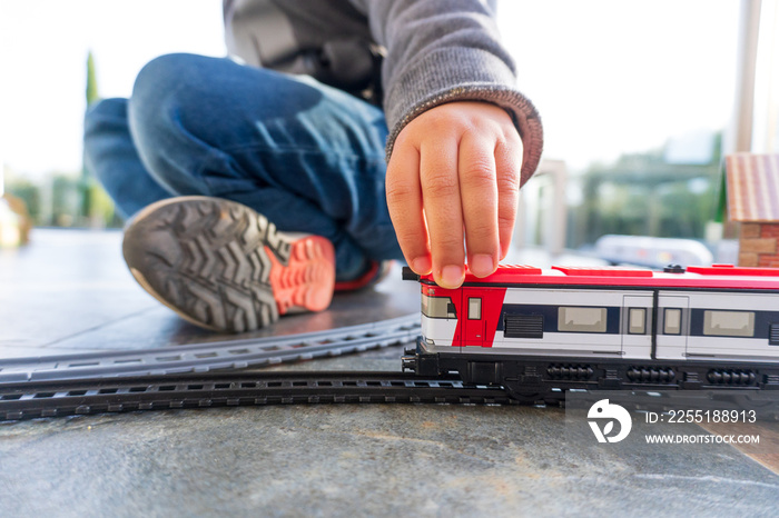 Young kid playing with toy trains on the floor. Toy train similar to Cercanias Renfe Spanish train and Ave high speed train