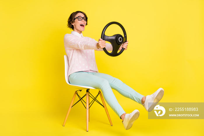 Full body photo of brown bob haired girl sit hold steering wheel amazed speed wear green pants isolated on yellow color background