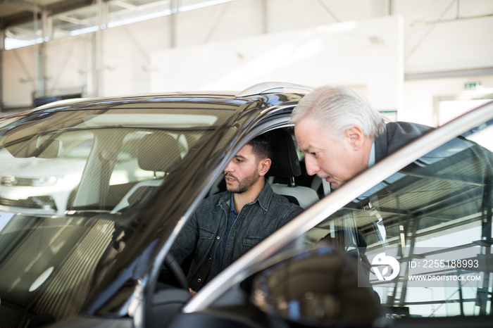 Happy young family talking to the salesman and choosing their new car in a showroom