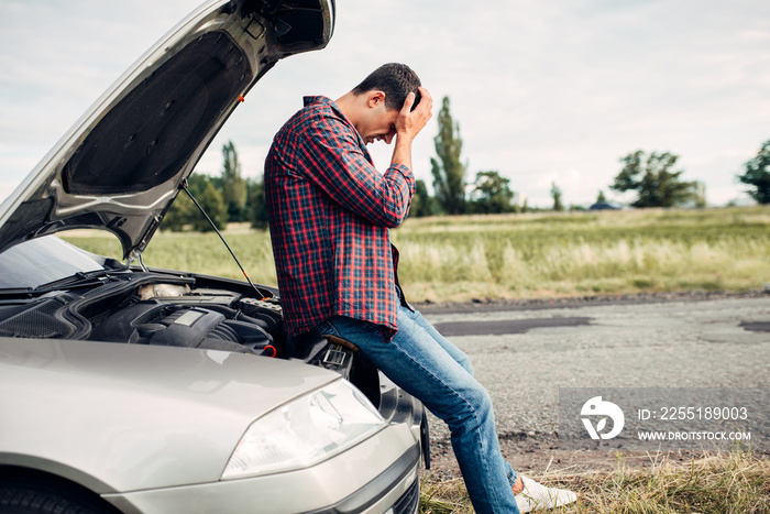 Depressed man sitting on a hood of broken car