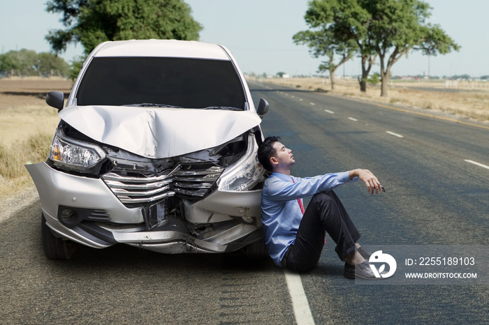 Frustrated businessman sitting near a broken car