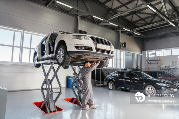 Mechanic repairing Car on lift in mechanic shop or garage, interior of auto repair workshop