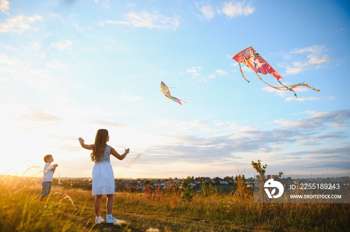 Happy children launch a kite in the field at sunset. Little boy and girl on summer vacation.