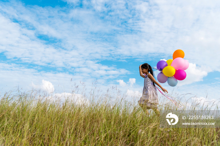 Cheerful cute girl holding balloons running on green meadow white cloud and blue sky with happiness. Hands holding vibrant air balloons play on birthday party happy times summer on sunlight outdoor