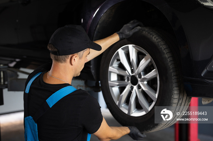 Auto mechanic checking suspension of a lifted car. Experienced car service technician working at the garage. Mechanic repairing car at his workshop. Car on a lift in a specialized service.