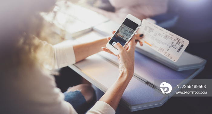 Enjoying business travel concept. Young beautiful brunette tourist girl travelling on the train sitting near the window using smartphone,holding ticket hands.