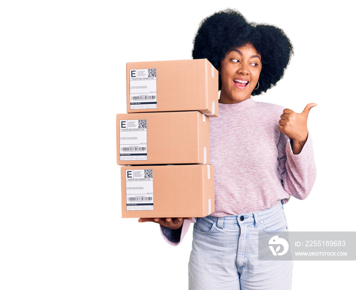 Young african american girl holding delivery package pointing thumb up to the side smiling happy with open mouth