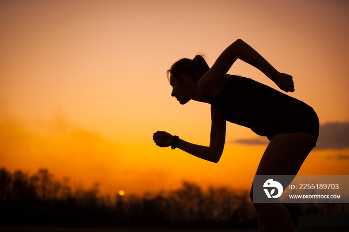 Silhouette of running woman starting run at sunset with sky in the background