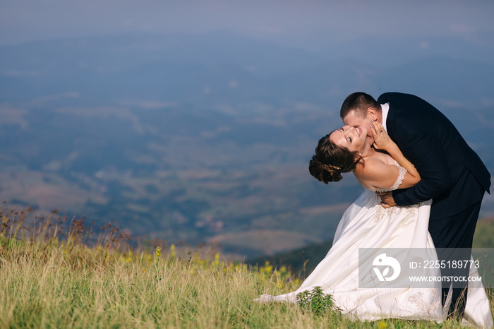 The bride and groom on the background of the mountains. The man kisses the bride on the neck.