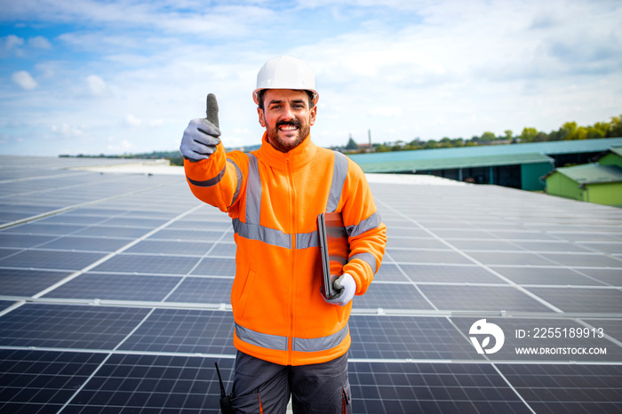 Portrait of professional solar company worker holding thumbs up on the rooftop after successful solar panels installation.