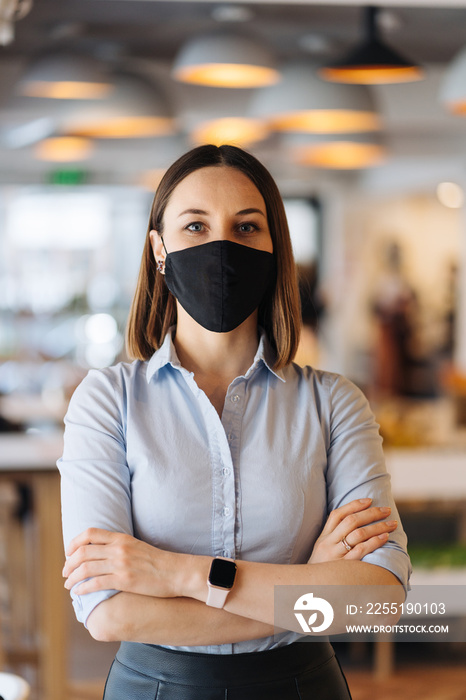 Woman business owner wearing face mask after reopening restaurant, arms folded