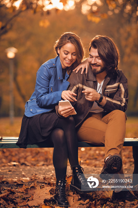 Young couple using cellphone in autumn colored park.