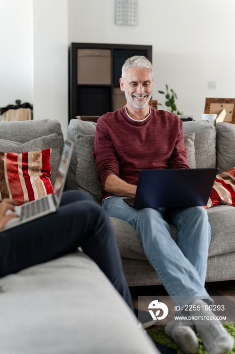 Smiling male couple working on laptops on sofa at home