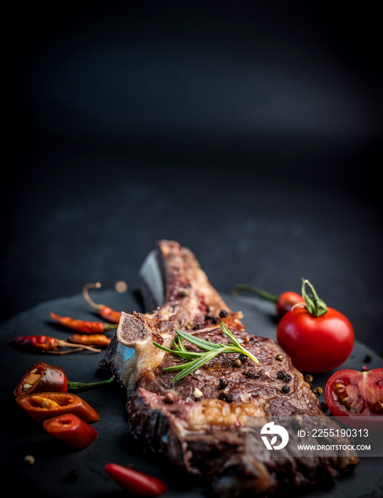 Close-up of grilled beef steak on bone with tomatoes on the stone cutting board with copy space