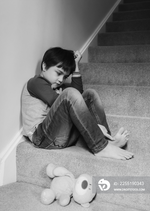 Sad boy wearing  sitting on carpet staircase in the morning, Lonely kid looking dow with sad face not happy to go back to school, Depressed child boy is sitting in the corner of a stair. Mental health