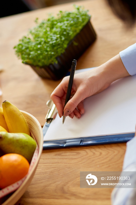 Nutritionist, dietitian woman writing a diet plan, with healthy vegetables and fruits