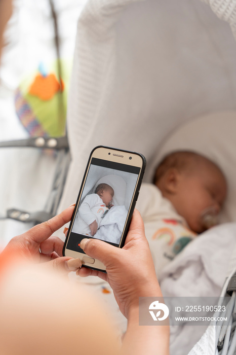 Mother photographing newborn baby girl sleeping in crib