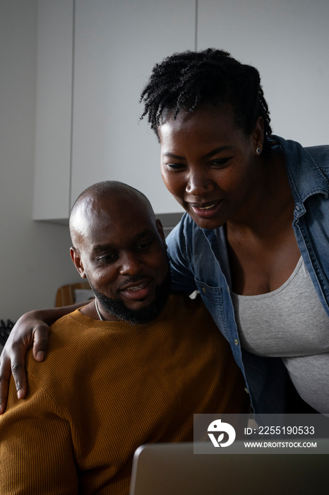 Man and pregnant woman looking at laptop in kitchen