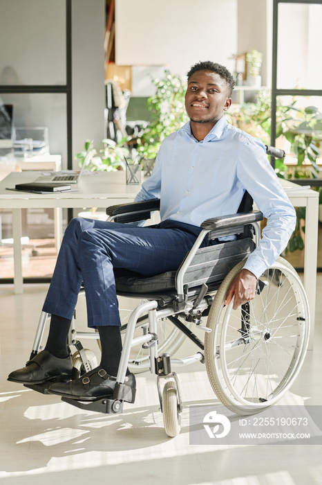 Portrait of African young businessman sitting in wheelchair at office and smiling at camera