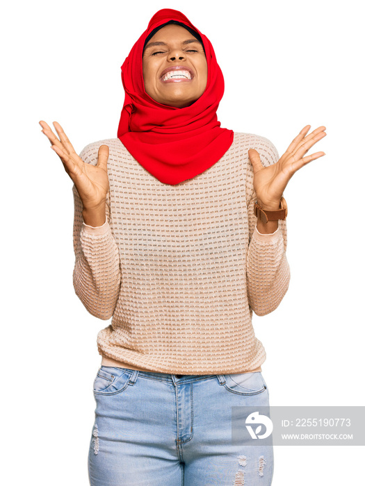 Young african american woman wearing traditional islamic hijab scarf celebrating mad and crazy for success with arms raised and closed eyes screaming excited. winner concept