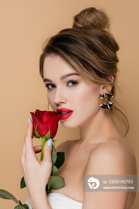 young and sensual woman with bare shoulders posing with rose near red lips isolated on beige.