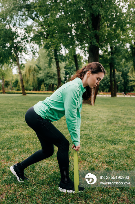 Side view of sportswoman pulling up resistance band in park