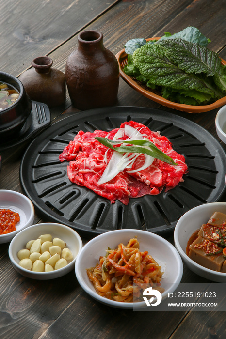 Bulgogi, a traditional Korean food on a black stone plate with a wooden background, and side dishes 나무배경에 검은 돌판위에 있는 한국 전통 음식인 불고기와 밑반찬