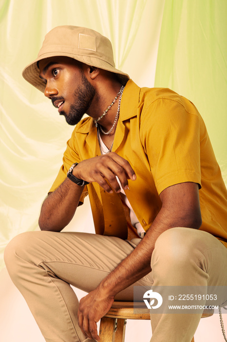 Malaysian Indian man posed in front of a cloth background, styled in a yellow shirt and hat