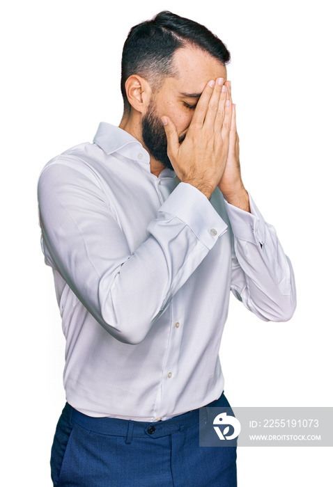 Young man with beard wearing business shirt with sad expression covering face with hands while crying. depression concept.